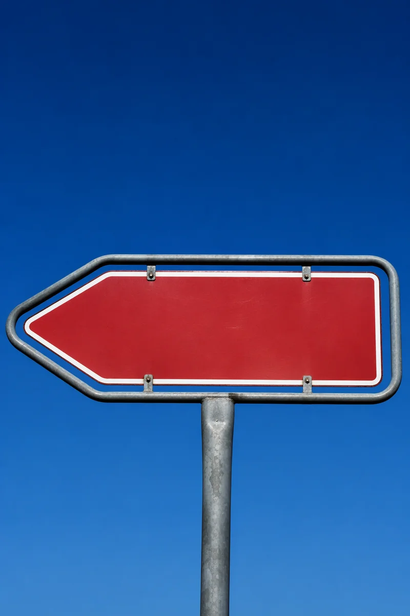 Red Left Arrow Sign Against Blue Sky