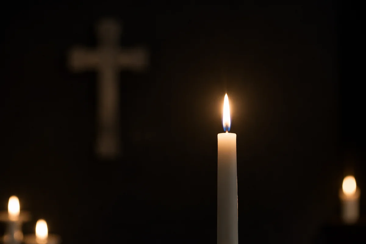 Burning Candle with Cross in Darkness