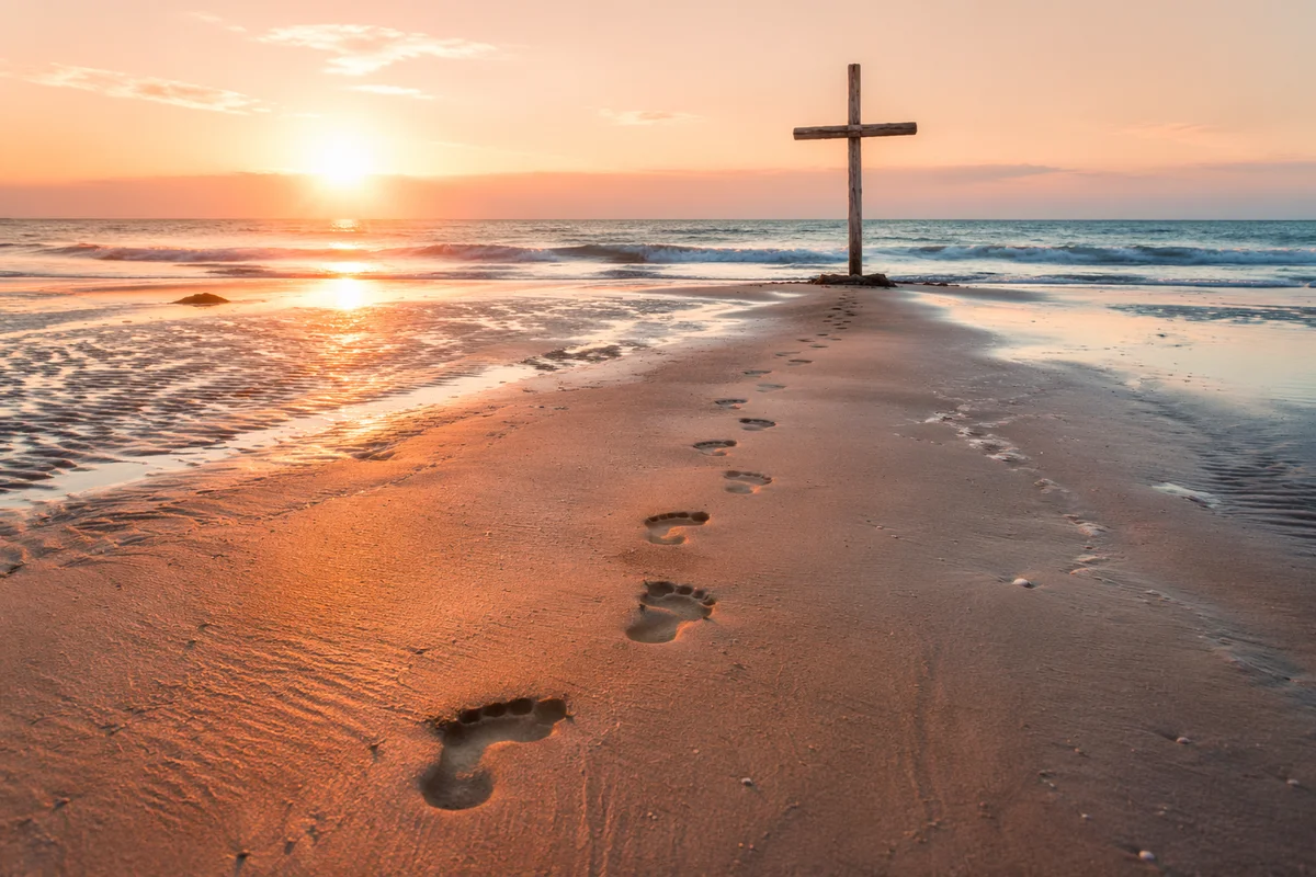 Footprints Leading to Driftwood Cross at Sunrise
