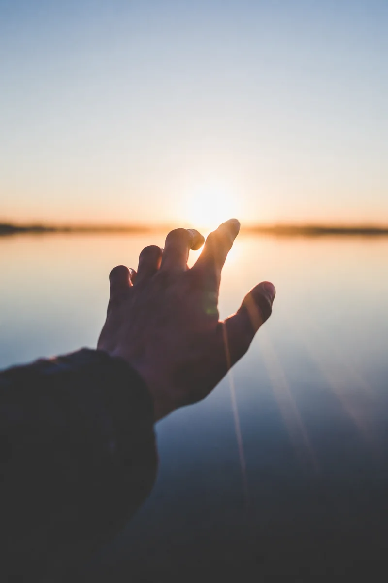 Hand Reaching Toward Sunrise Light