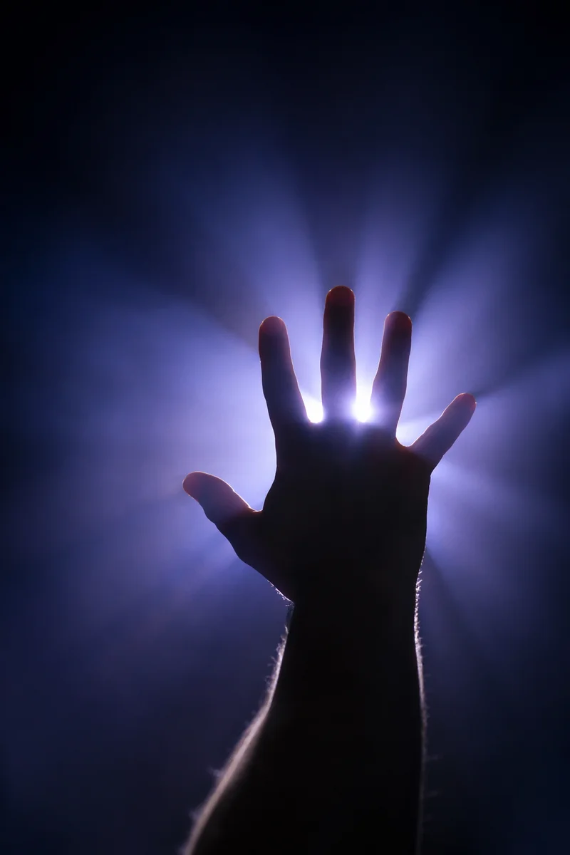 Silhouetted Hand Reaching Toward Divine Light