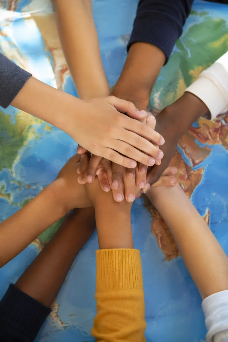 Children Stacking Hands Over Classroom Map