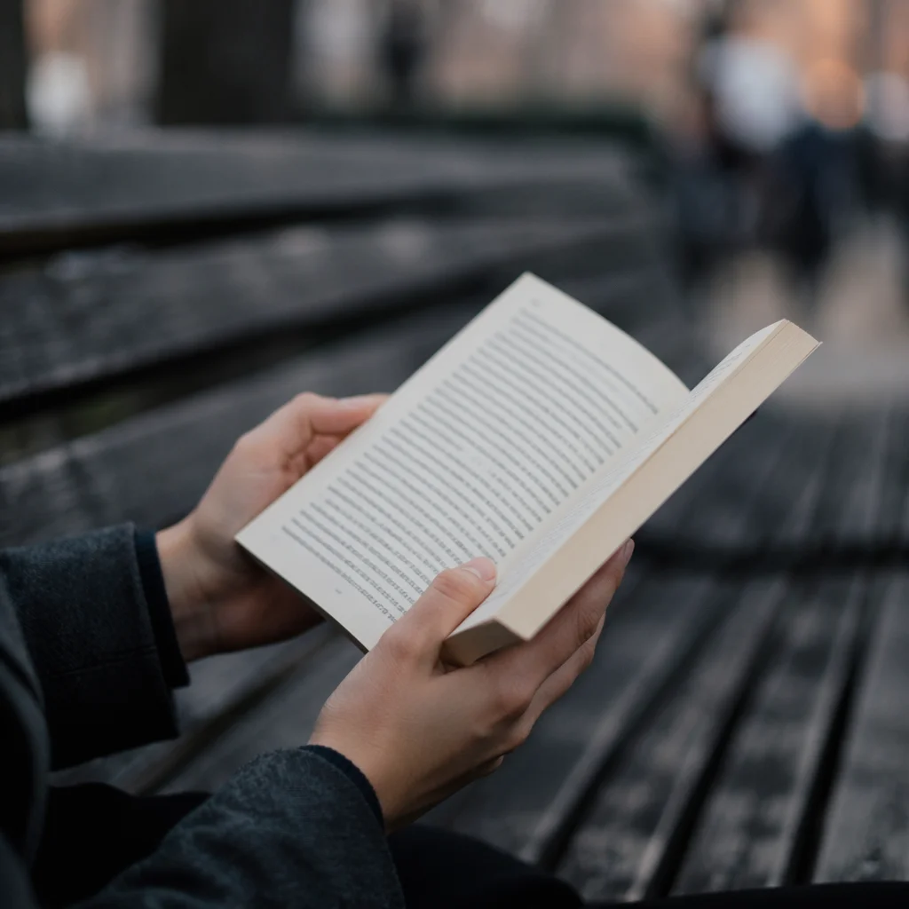 Hands Reading Open Book on Park Bench
