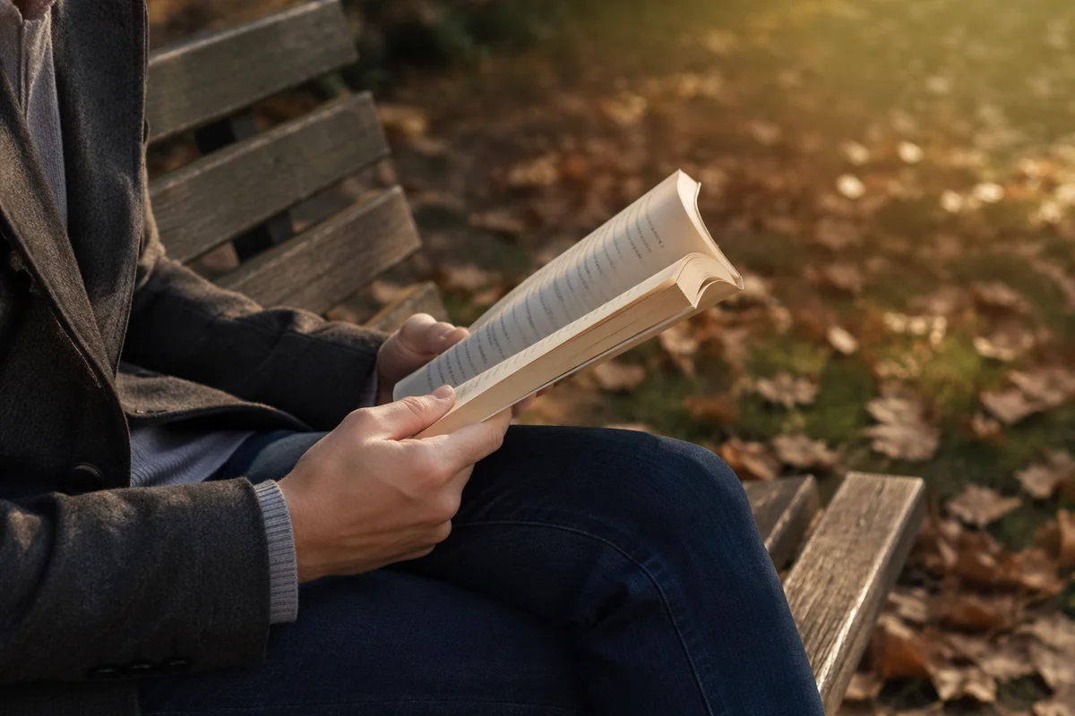 Hands Holding Open Book on Park Bench