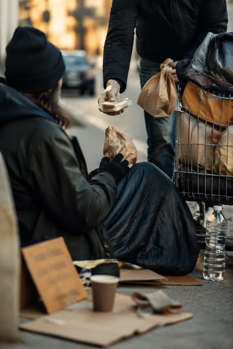 Volunteer Offering Food on City Sidewalk