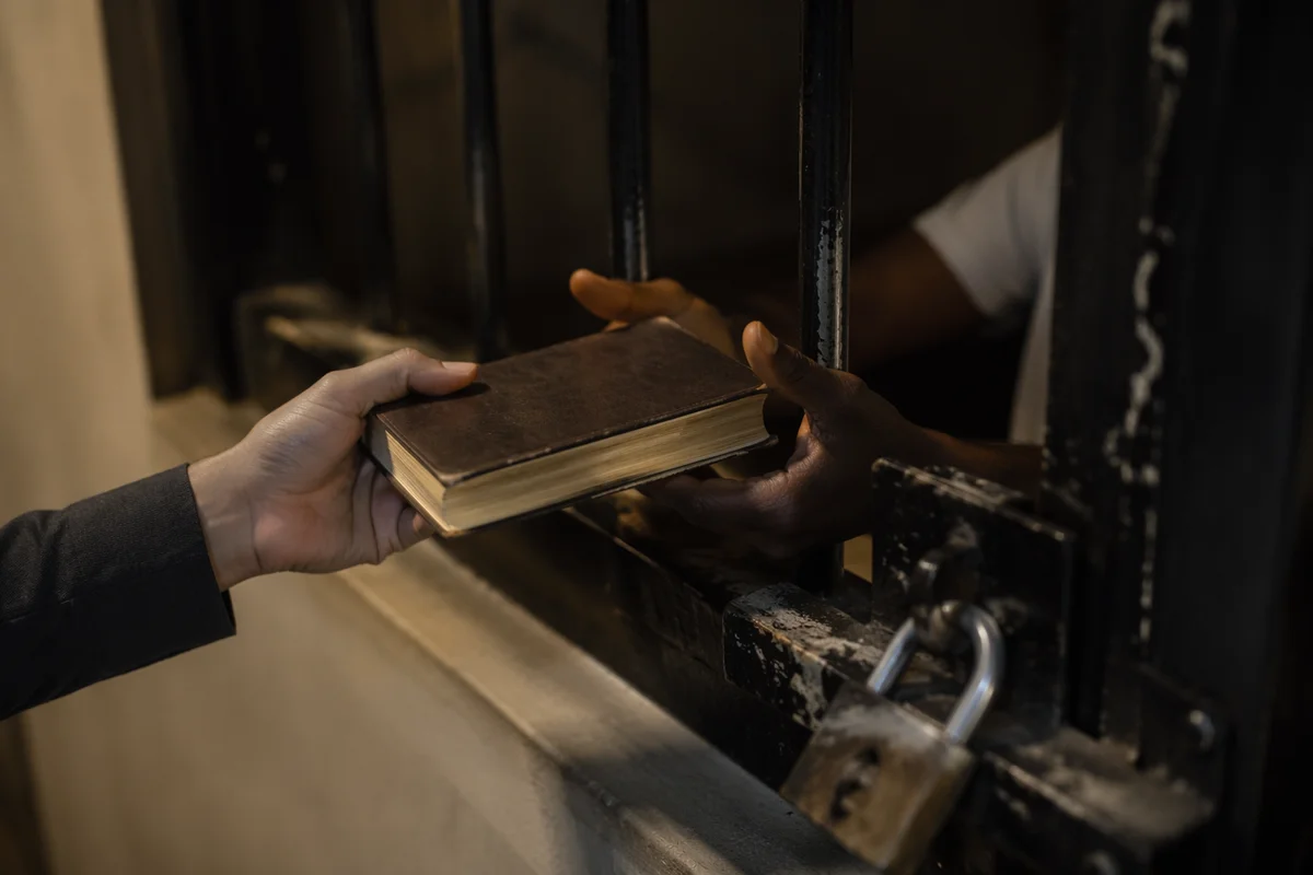 Hands Exchanging Bible Through Prison Bars