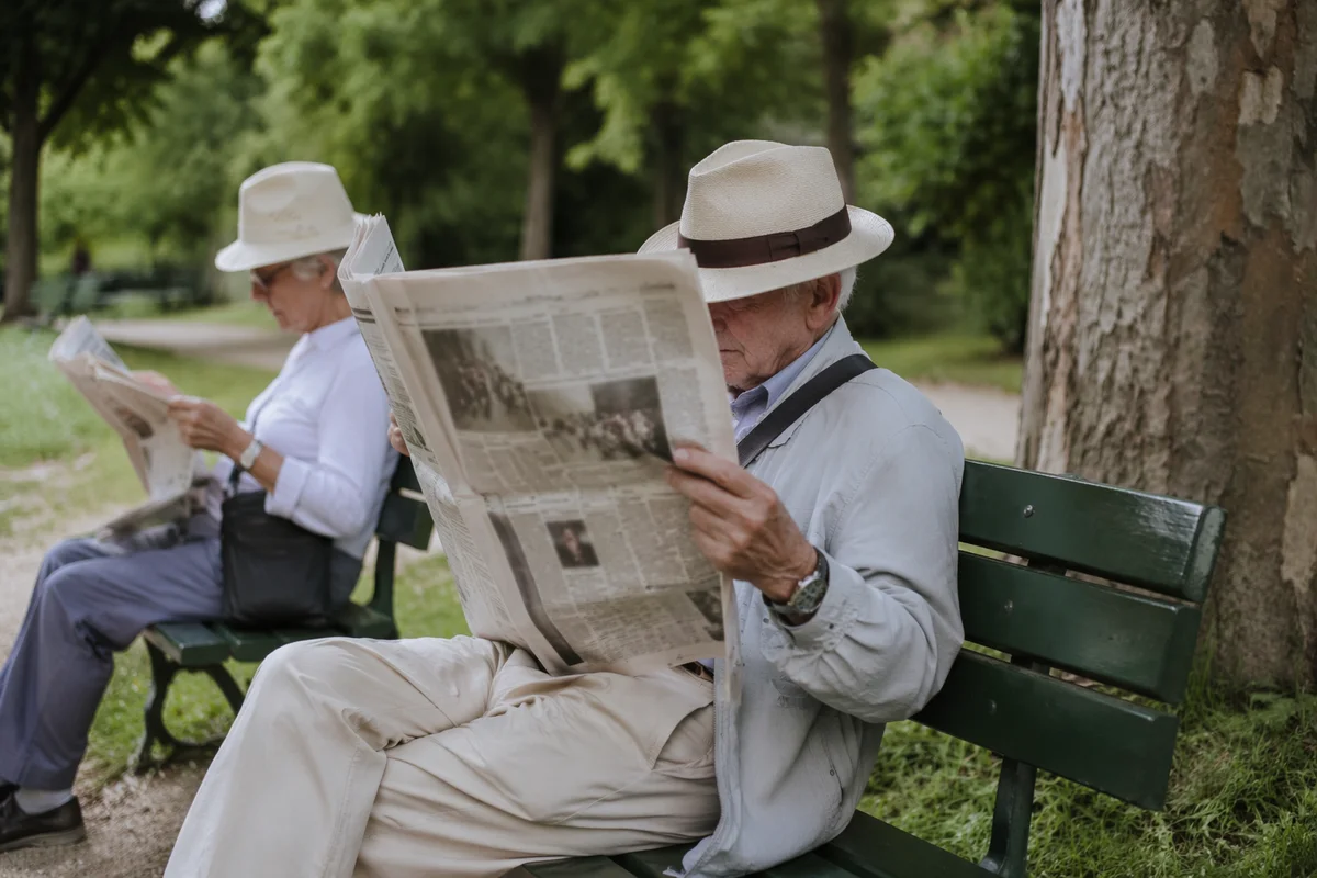 Elderly Man Reading Newspaper on Park Bench