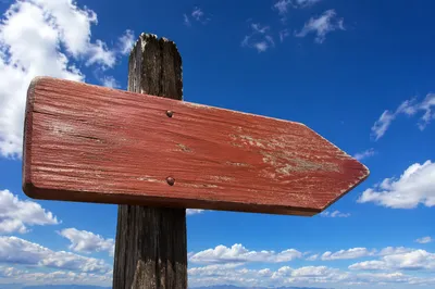 Red Wooden Arrow Sign Under Blue Sky