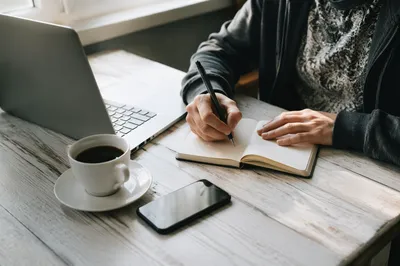 Focused Student Writing Notes Beside Laptop