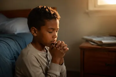 Young Boy Praying Beside Bed at Dawn