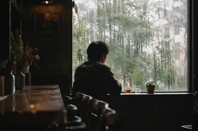 Solitary Figure Watching Rain Through Cafe Window
