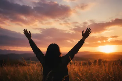 Silhouetted Figure Raising Hands at Sunset