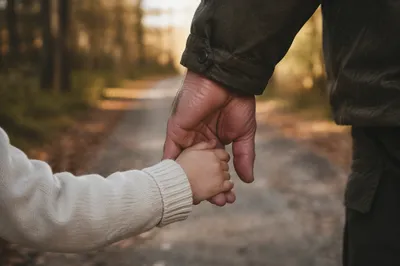 Child Holding Adult Hand on Sunlit Path