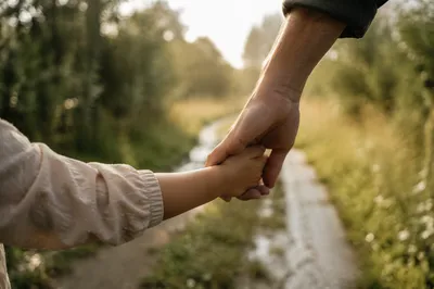 Child Holding Adult Hand on Rainy Path