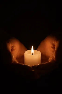 Hands Holding Candle Flame in Darkness