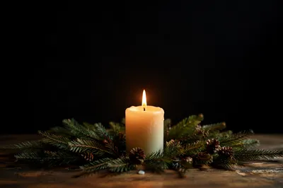 Burning Candle with Evergreen in Darkness