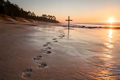 Footprints Leading to Driftwood Cross at Sunrise