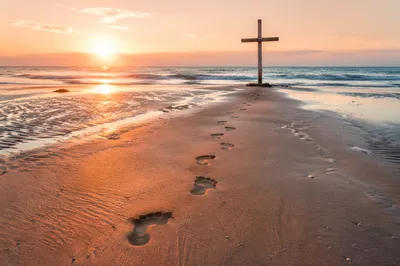 Footprints Leading to Driftwood Cross at Sunrise
