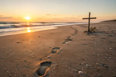 Footprints Leading to Driftwood Cross at Sunrise
