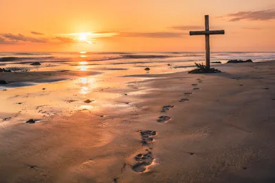 Footprints Leading to Driftwood Cross at Sunrise