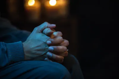 Folded Hands in Candlelit Prayer