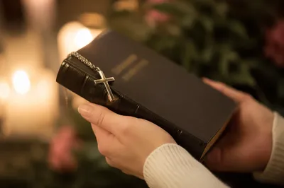 Hands Holding Bible with Cross Pendant