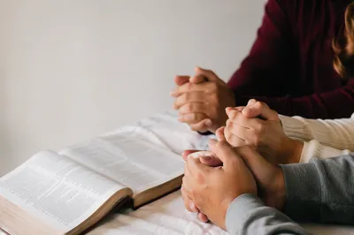 Clasped Hands Beside Open Devotional Book