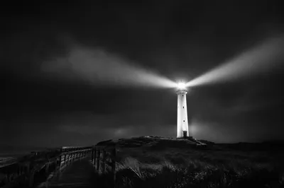 Stormlit Lighthouse Beacon Over Rocky Coast