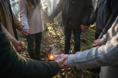Prayer Group Hands Around Lantern in Evergreen Grove