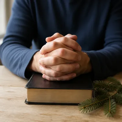 Praying Hands on Bible with Evergreen Sprig