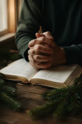 Praying Hands Over Bible with Evergreen