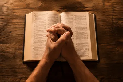 Praying Hands Over Open Bible