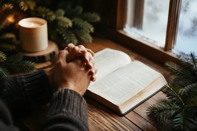 Praying Hands Beside Bible and Evergreens