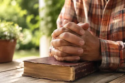 Praying Hands Resting on Worn Bible