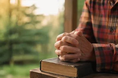Praying Hands Resting on Bible by Window