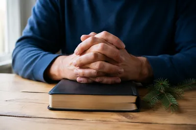 Praying Hands on Bible with Evergreen Sprig