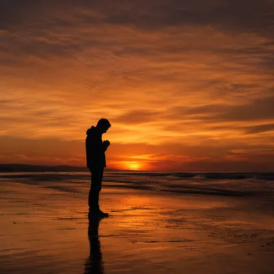 Silhouette Praying on Shoreline at Sunset