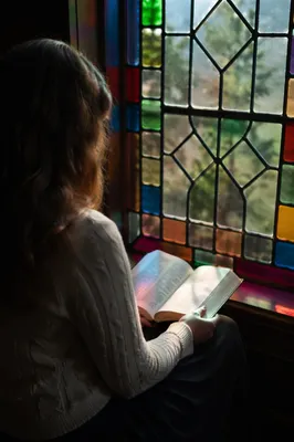Woman Reading Bible by Stained Glass Window