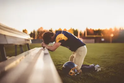 Kneeling Athlete Praying at Sunrise Field
