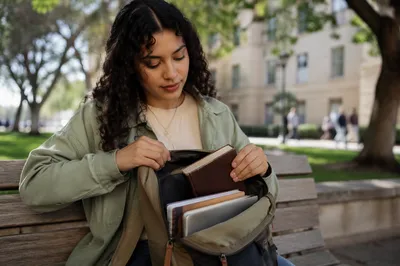 Student Opening Backpack on Campus Bench