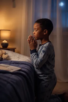 Young Child Praying Beside Bed at Night