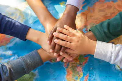 Children Stacking Hands Over Classroom World Map