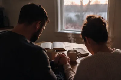Couple Praying Together at Sunrise Kitchen Table