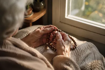Elderly Hands Holding Wooden Rosary in Morning Light