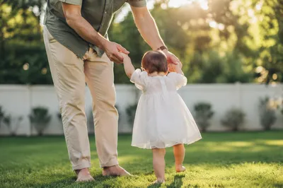 Father Helping Toddler Walk in Backyard
