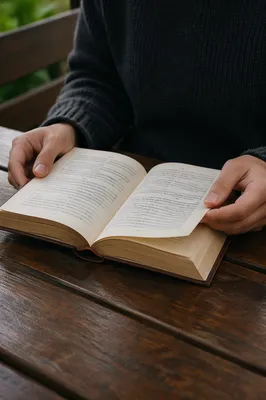 Hands Holding Open Book on Outdoor Bench