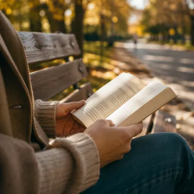 Hands Holding Open Book on Park Bench