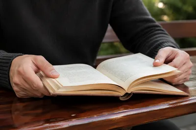 Hands Holding Open Book on Outdoor Bench
