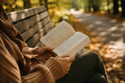 Hands Holding Open Book on Park Bench