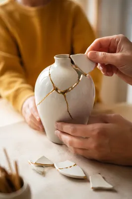 Hands Repairing White Vase With Gold Kintsugi